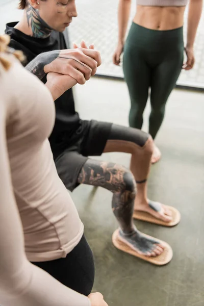 Татуйований чоловік сидить на стільці, одягаючи голі ноги на дошку Садху біля жінок в студії йоги — стокове фото