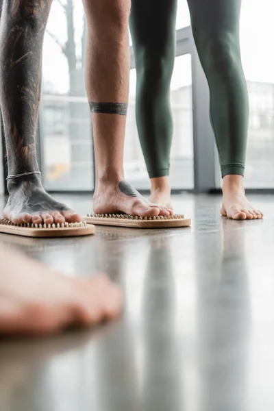 Cropped view of tattooed man standing with bare feet on nail board near woman in yoga studio — Stock Photo