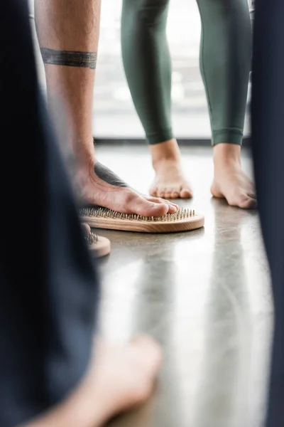 Cropped view of man with tattoo on legs standing on nail board near people in yoga studio — Stock Photo