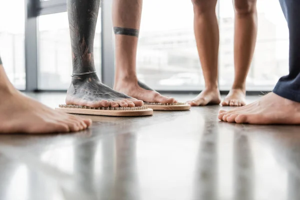 Частичный вид босоногого человека с татуированными ногами, стоящего на ногтевой доске рядом с людьми — стоковое фото