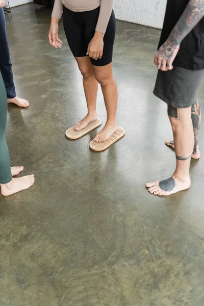 Vista recortada de la mujer tatuada de pie en el tablero de uñas sadhu cerca de personas en el estudio de yoga - foto de stock