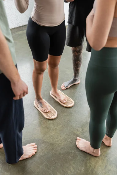 Vista ritagliata della donna tatuata in piedi sul bordo del chiodo sadhu vicino alle persone in studio di yoga — Foto stock