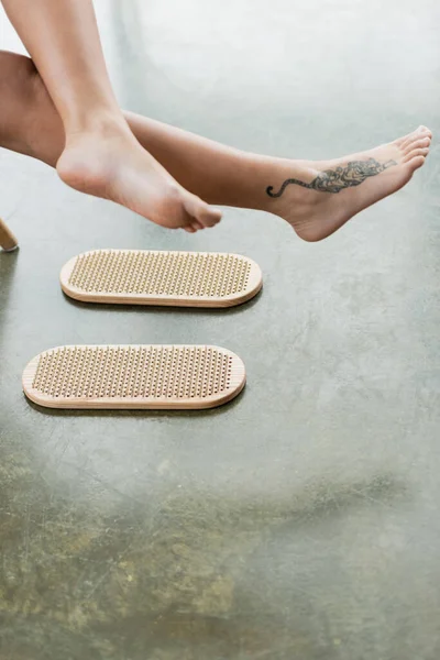 Partial view of tattooed woman showing bare feet near sadhu board in yoga studio — Stock Photo