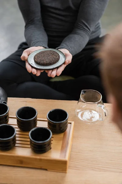Vista ritagliata di uomo in possesso di tè puro compresso vicino a teiera di vetro e tazze da tè tradizionali — Foto stock