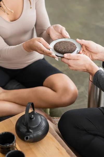 Vista recortada del hombre dando plato con té puer comprimido a mujer en estudio de yoga - foto de stock