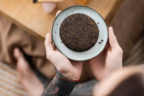 Top view of tattooed man holding plate with compressed chinese puer tea — Stock Photo