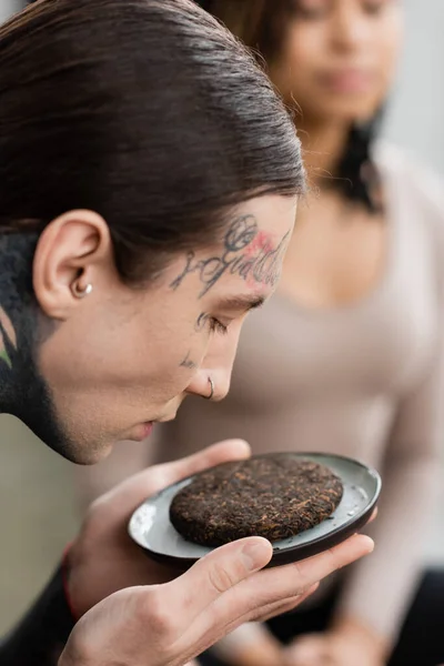 Giovane e tatuato uomo odore fermentato tè puer vicino donna afro-americana su sfondo sfocato — Foto stock