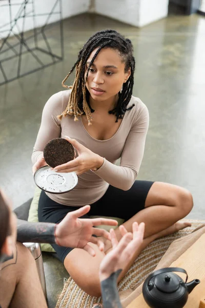 Junge afrikanisch-amerikanische Frau mit Dreadlocks zeigt tätowiertem Mann im Yogastudio komprimierten Puertee — Stockfoto