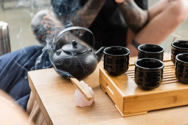 Verbrennung von Palo Santo in der Nähe traditioneller chinesischer Teekannen und Tassen im Yoga-Studio — Stockfoto