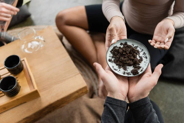 Top view of african american woman passing plate with fermented puer tea to man in yoga studio — Stock Photo