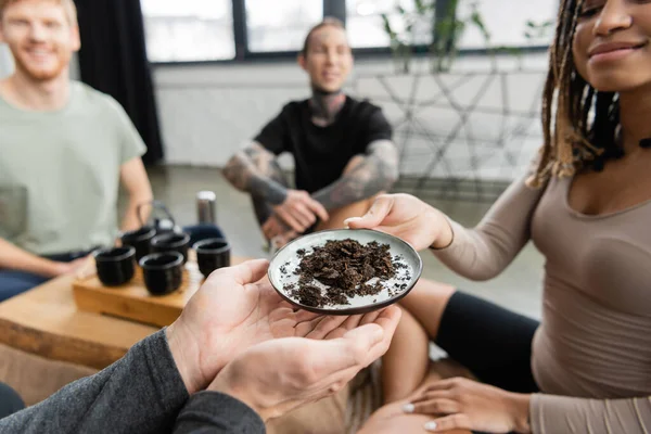 Donna afro-americana sorridente che passa piatto con tè puro fermentato all'uomo in studio di yoga — Foto stock