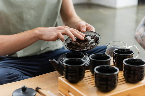 Vue recadrée de l'homme ajoutant du thé puer dans la théière japonaise traditionnelle près des tasses — Photo de stock