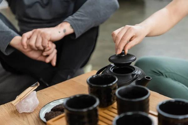 Обрізаний вид на жінку, що заварює чай у традиційному чайнику біля татуйованого чоловіка середнього віку — стокове фото