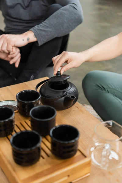 Abgeschnittene Ansicht einer Frau, die Tee in einer chinesischen Teekanne in der Nähe tätowierter Mann mittleren Alters braut — Stockfoto