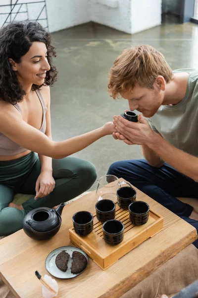 Curly middle eastern woman smiling while giving to smell puer tea to redhead man — Stock Photo