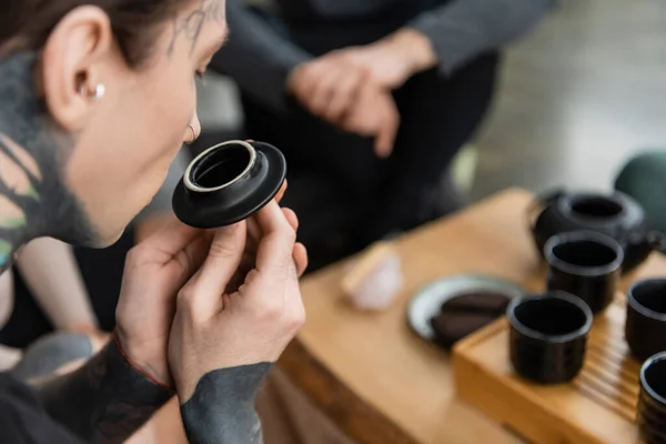 Tattooed young man smelling puer tea near Chinese cups in yoga studio — Stock Photo