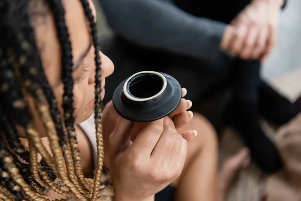 Overhead view of african american woman with dreadlocks smelling puer tea from teapot lid — Stock Photo