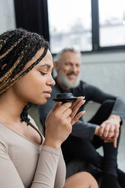 Giovane donna afroamericana con dreadlocks odore di tè puer vicino all'uomo di mezza età su sfondo sfocato — Foto stock