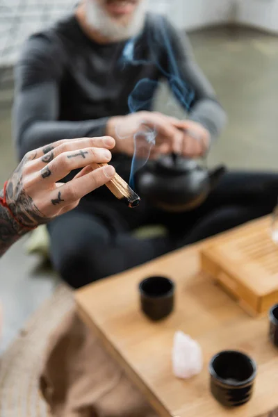 Обрезанный вид человека с татуировкой, держащего деревянный пало санто в студии йоги — стоковое фото