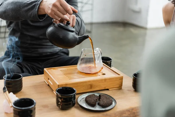 Vista cortada do homem derramando chá puer recém-fabricado em jarro de vidro — Fotografia de Stock