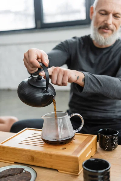Tattooed middle aged man pouring freshly brewed puer tea into glass jug — Stock Photo
