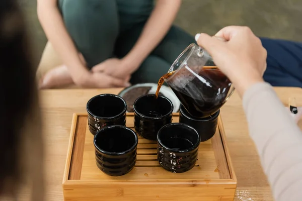 Vista ritagliata della donna versando puer da brocca di vetro in tazze da tè tradizionali — Foto stock