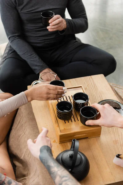 Cropped view of people taking traditional japanese cups with puer tea near teapot — Stock Photo