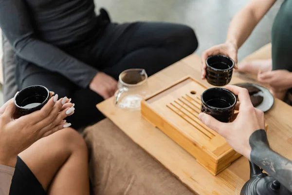 Teilansicht multiethnischer Menschen mit traditionellen chinesischen Tassen mit purem Tee im Yogastudio — Stockfoto
