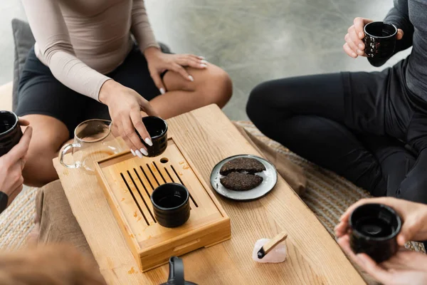 Cropped view of interracial people holding tea cups with puer near palo santo — Stock Photo
