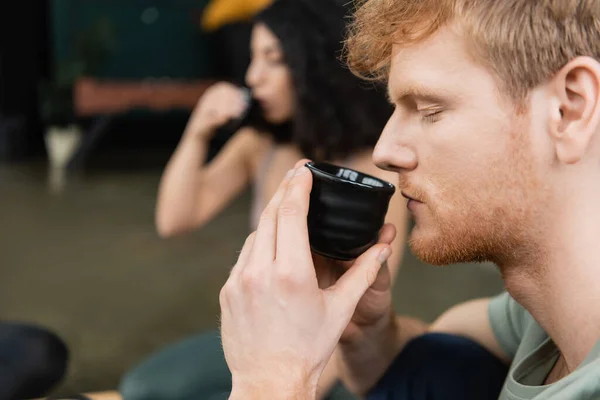 Side view of redhead man holding Chinese cup and smelling brewed puer tea — Stock Photo