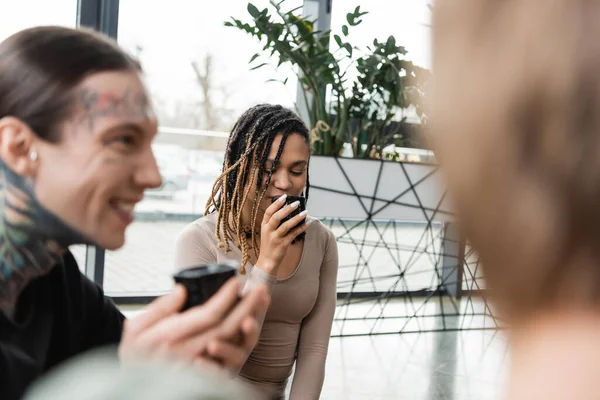 African american woman with dreadlocks drinking puer tea near tattooed man on blurred foreground — Stock Photo