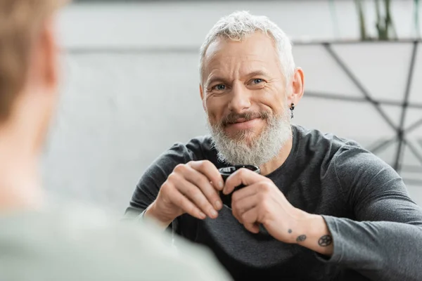 Happy middle aged man with tattoos holding Chinese cup with puer tea in yoga studio — Stock Photo