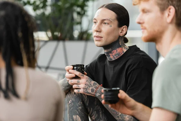 Tattooed man holding Japanese cup with tea near people on blurred foreground — Stock Photo