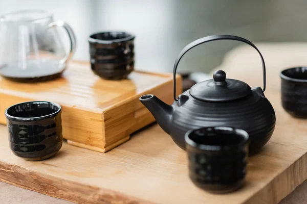 Théière japonaise traditionnelle près des tasses et cruche en verre avec du thé puer sur fond flou — Photo de stock