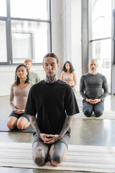 Мультиэтническая группа людей, медитирующих с закрытыми глазами в позе йоги Thunderbolt — стоковое фото