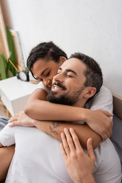 Татуйована афроамериканська жінка обіймає веселого бородатого хлопця в спальні вдома — стокове фото