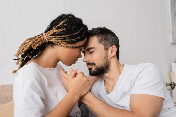 Бородатый мужчина и молодая африканская американка держатся за руки в спальне дома — стоковое фото