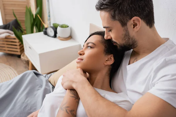 Dreamy african american woman looking away near bearded boyfriend in bedroom at home — Stock Photo