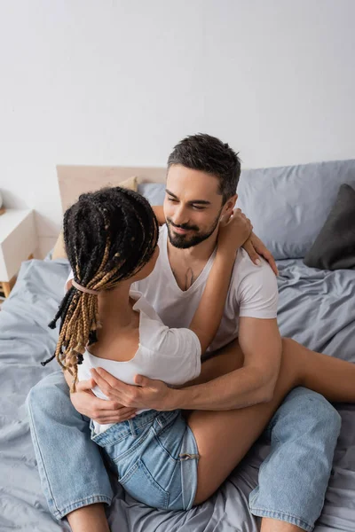 Aus der Vogelperspektive: glücklicher bärtiger Mann und afrikanisch-amerikanische Frau mit Dreadlocks, die sich zu Hause auf dem Bett umarmen — Stockfoto