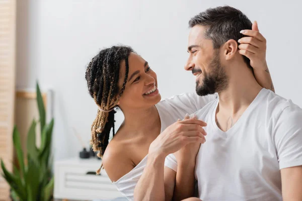 Joyful african american woman and bearded man smiling at each other in bedroom at home — Stock Photo