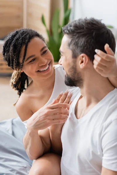 Cheerful african american woman with dreadlocks looking at blurred boyfriend in bedroom at home — Stock Photo