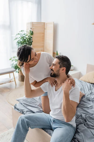 Alegre interracial casal em branco t-shirts olhando para o outro enquanto se divertindo no quarto em casa — Fotografia de Stock