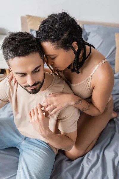 Высокий угол зрения бородатый мужчина трогает руку горячей африканской американки в нижнем белье в спальне на дому — стоковое фото
