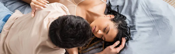 Vista superior do homem morena em t-shirt perto de mulher americana africana quente com olhos fechados na cama em casa, banner — Fotografia de Stock