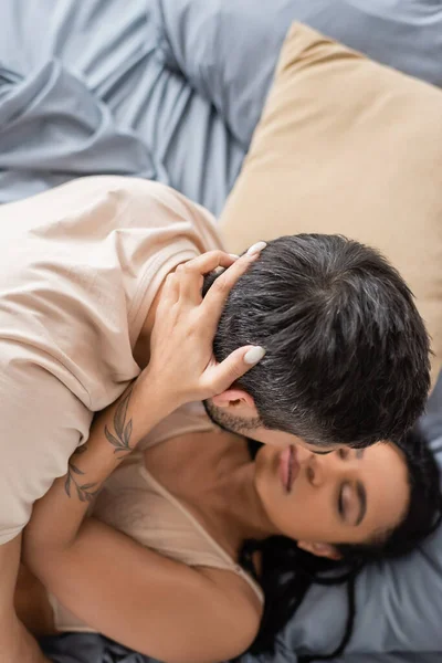Вид зверху сексуальна афроамериканська жінка з закритими очима обіймає брюнетку чоловіка в футболці в спальні вдома — стокове фото