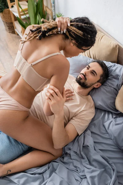 High angle view of passionate african american woman with dreadlocks seducing bearded man lying on bed at home — Stock Photo