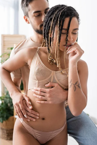 Blurred man embracing sexy african american woman in underwear standing with closed eyes in bedroom at home — Stock Photo
