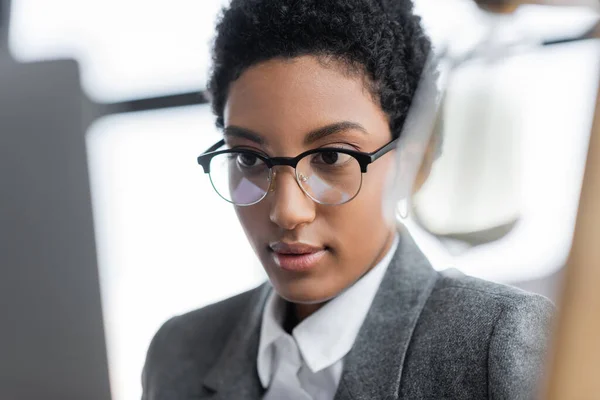 Retrato de la joven mujer de negocios afroamericana en chaqueta gris y anteojos que trabajan en la oficina - foto de stock
