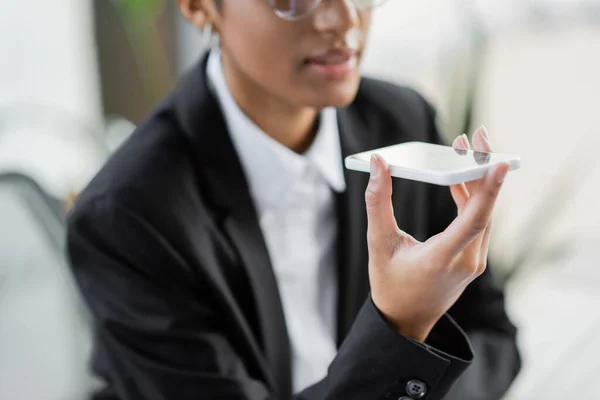 Partial view of blurred african american businesswoman sending voice message on smartphone while working in office — Stock Photo