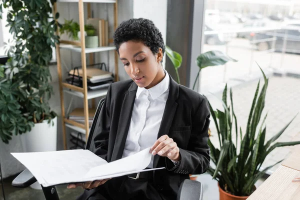 Молода афроамериканська бізнесменка в стильному офіційному одязі працює з документами в папці на посаді. — стокове фото
